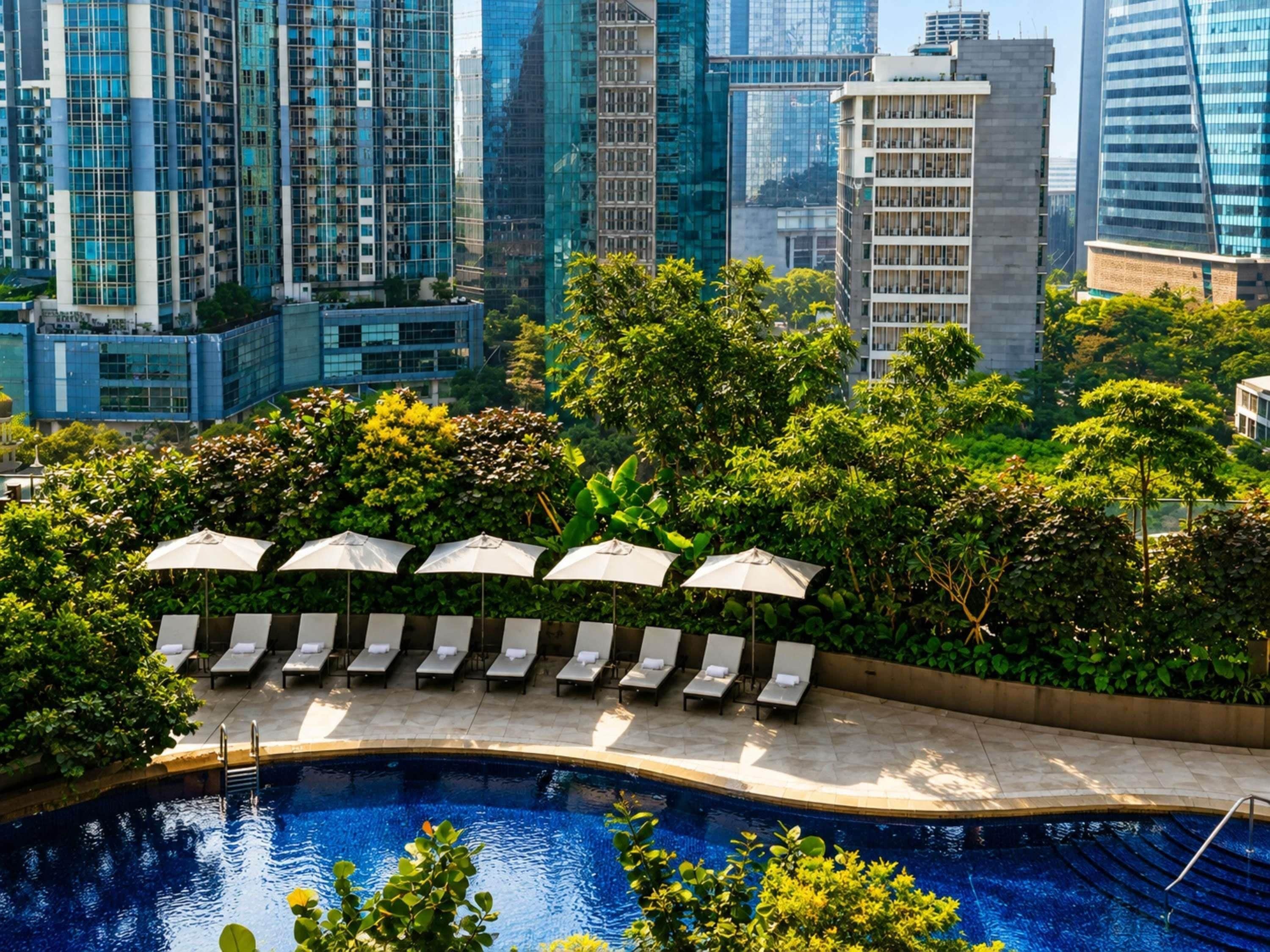 A rooftop pool with lounge chairs and umbrellas, surrounded by greenery and modern buildings.