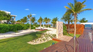 A resort with a wooden deck, palm trees, and a sandy beach area. - Oceanview Penthouse with Rooftop Plunge Pool & BBQ (Cancún)