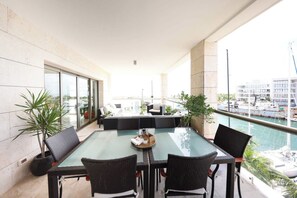 Ein Balkon mit Glastisch und Stühlen, der auf einen Yachthafen mit Booten blickt.