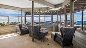 A covered outdoor area with wicker furniture and large windows offering a view of the beach and buildings. - Huge 6 Bdrm/6+ Ba Private GF Home, Pool, Dune Walkover, Easy Access, Gulf Views (Gulf Shores)