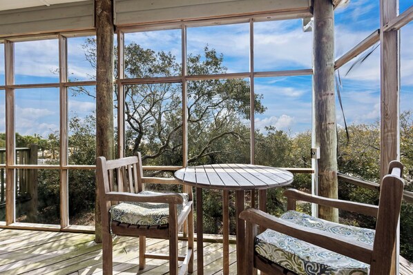 A wooden deck with a round table and two chairs, large windows offering a view of trees and sky. - Huge 6 Bdrm/6+ Ba Private GF Home, Pool, Dune Walkover, Easy Access, Gulf Views (Gulf Shores)