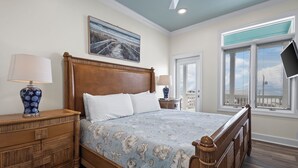 A bedroom with a wooden bed, a nightstand with a lamp, a window with blinds, and a painting on the wall.