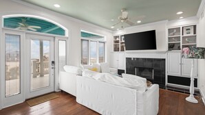 A spacious living room with a white sofa, a fireplace, a television, and a ceiling fan.