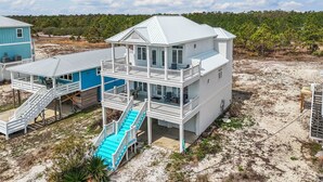 A multi-story beachfront property with a covered patio, outdoor seating, and a staircase leading to the upper levels.