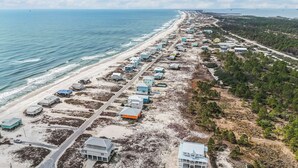 An aerial view of a coastal area with multiple beachfront properties, roads, and a beach.