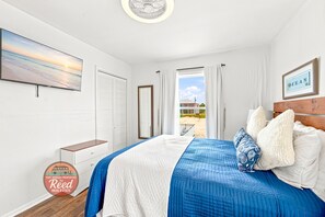 Un dormitorio con cama, ventana con cortinas, un cuadro en la pared y un marco con la palabra 'OCEAN'.