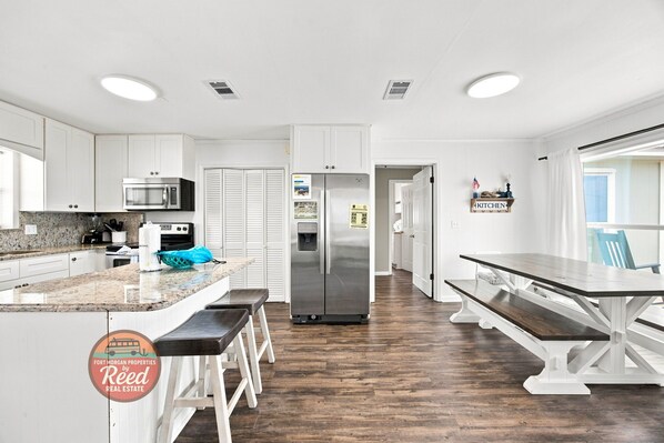 A modern kitchen with white cabinets, a stainless steel refrigerator, a microwave, and a granite countertop.