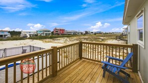 Terraza de madera con vista a una playa y algunas casas.