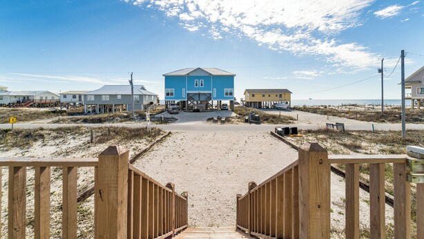 Ein Anwesen am Strand mit einem markanten, blauen Gebäude, einem Sandstrand und einem hölzernen Steg, der zum Eingang führt.