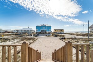 A beachside property with a prominent blue building, a sandy beach, and a wooden walkway leading to the entrance.