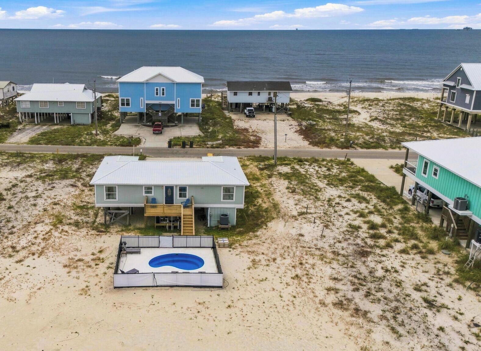 A beachfront property with multiple houses, a swimming pool, and a view of the ocean.