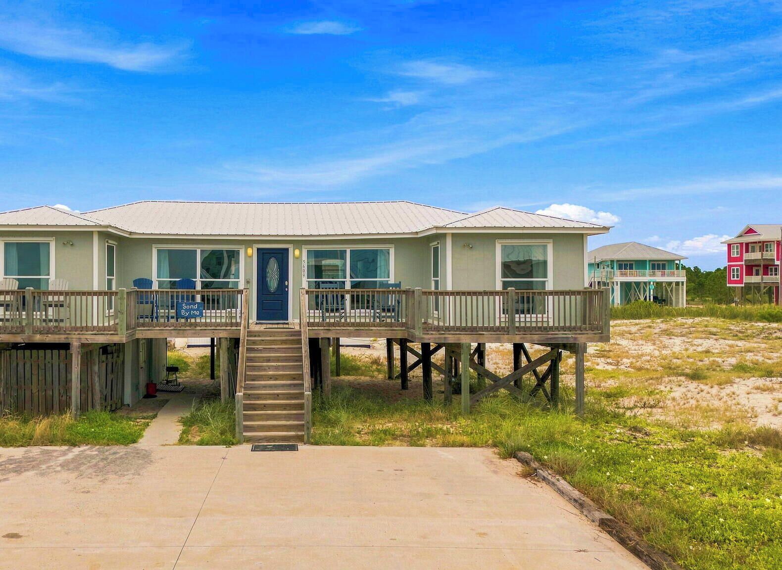 A beachfront property with a main building and a smaller structure, both elevated on stilts, with a clear sky above.