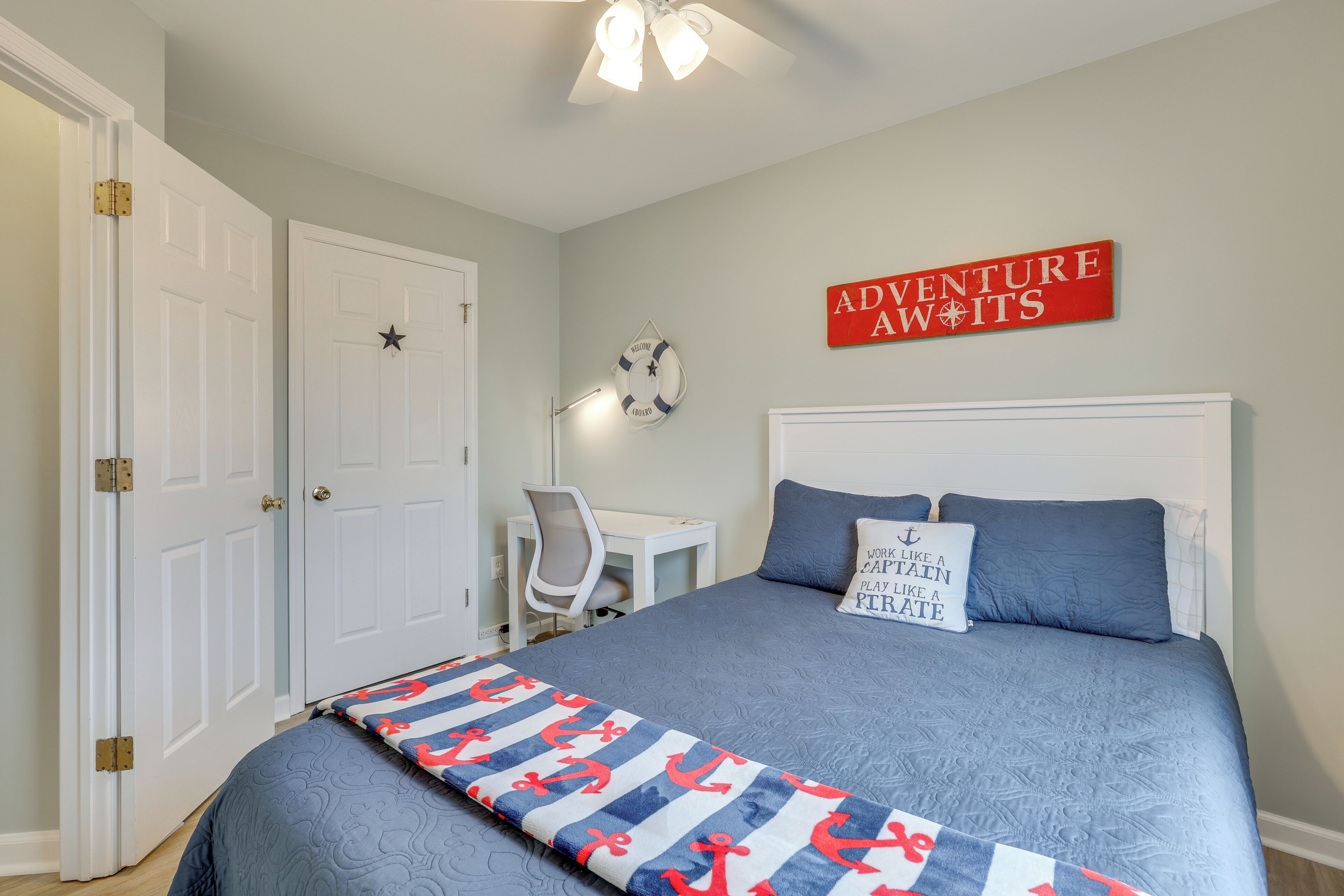 Un dormitorio con cama, escritorio y silla. Hay un cartel en la pared que dice 'ADVENTURE AWITS'.