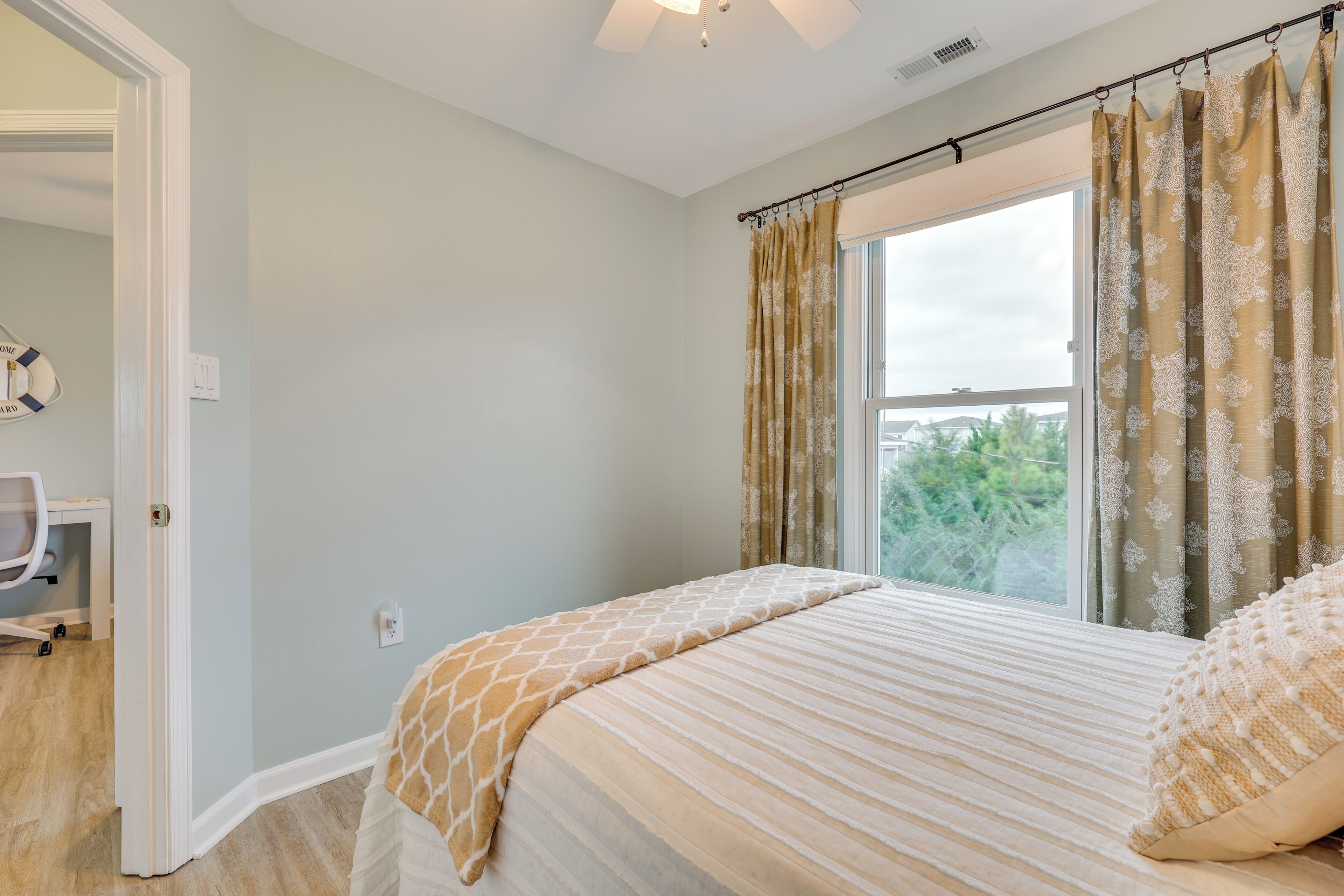 A bedroom with a bed, a window with curtains, a door, and a chair.