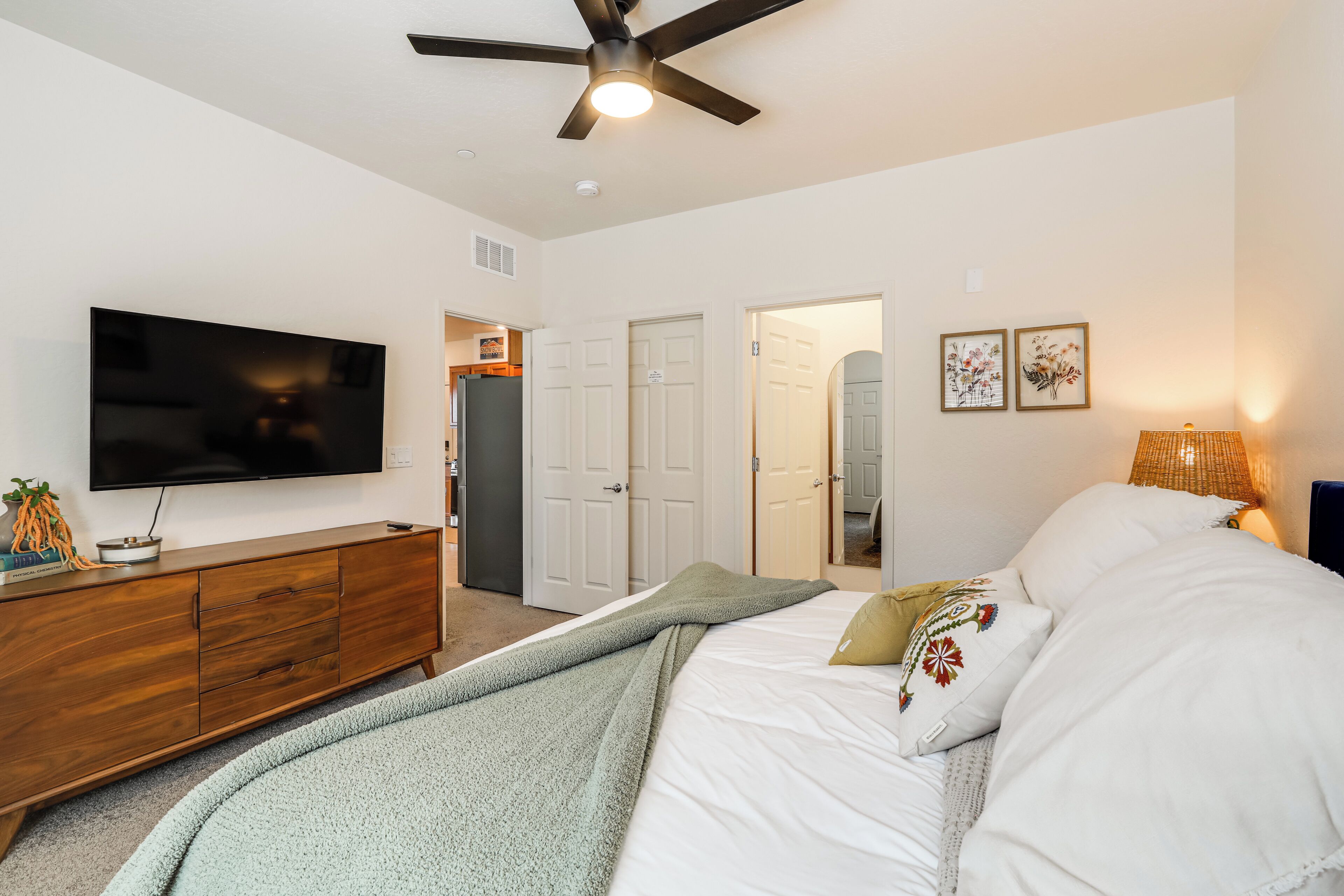 Une chambre à coucher avec un lit, une télévision, un ventilateur de plafond et une commode.