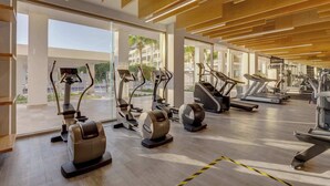 Ett modernt gym med olika typer av träningsutrustning, stora fönster och ett träpanelat tak.