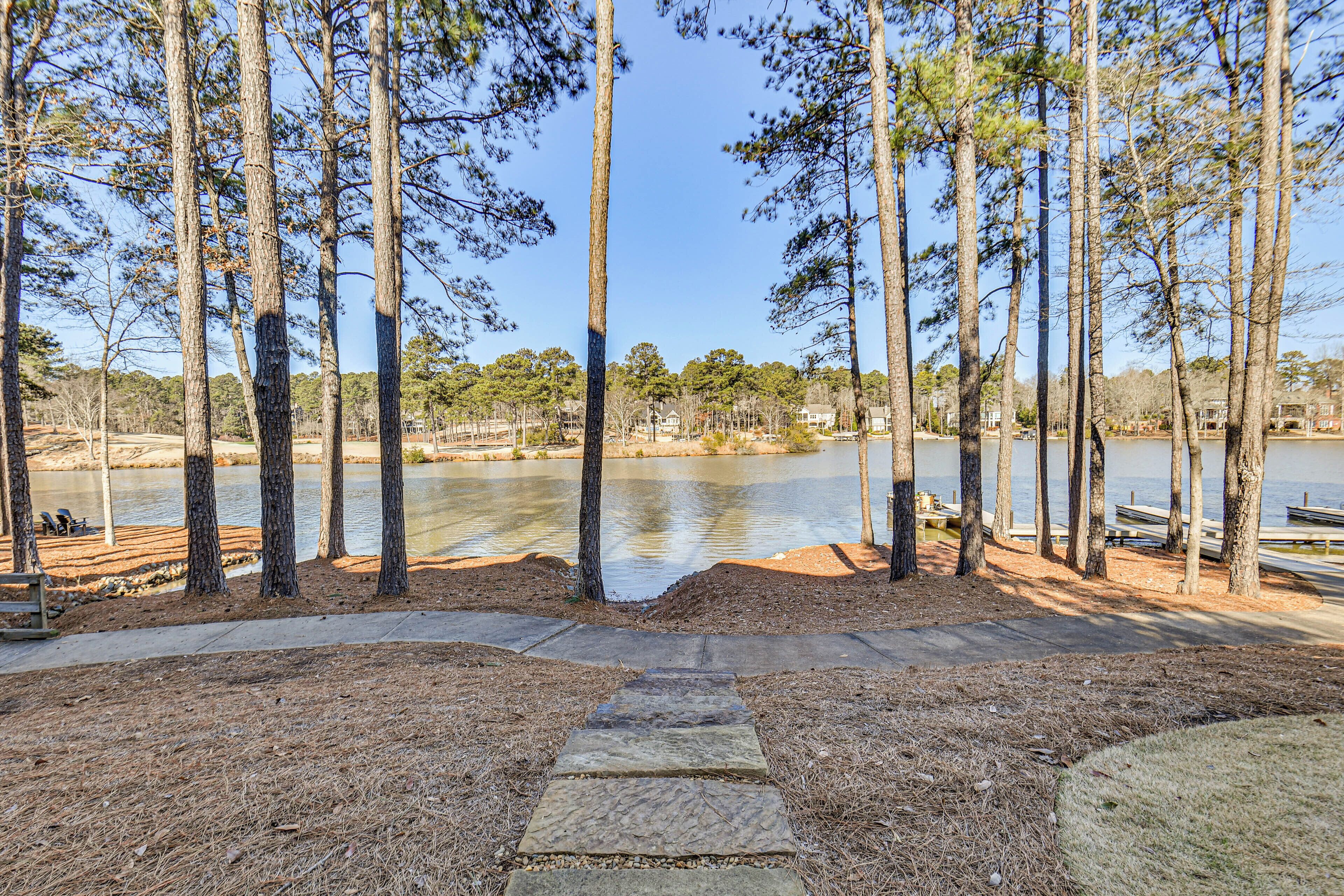 A lakeside park with tall pine trees, a stone pathway, and a view of a lake.