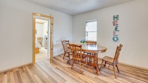 A dining area with a wooden table and chairs, a window with blinds, and a door leading to another room. - Mountain Views: Peaceful Aguilar Getaway! (Aguilar)
