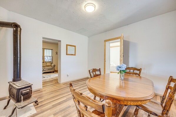 A dining area with a wooden table and chairs, a wood-burning stove, and a door leading to another room.