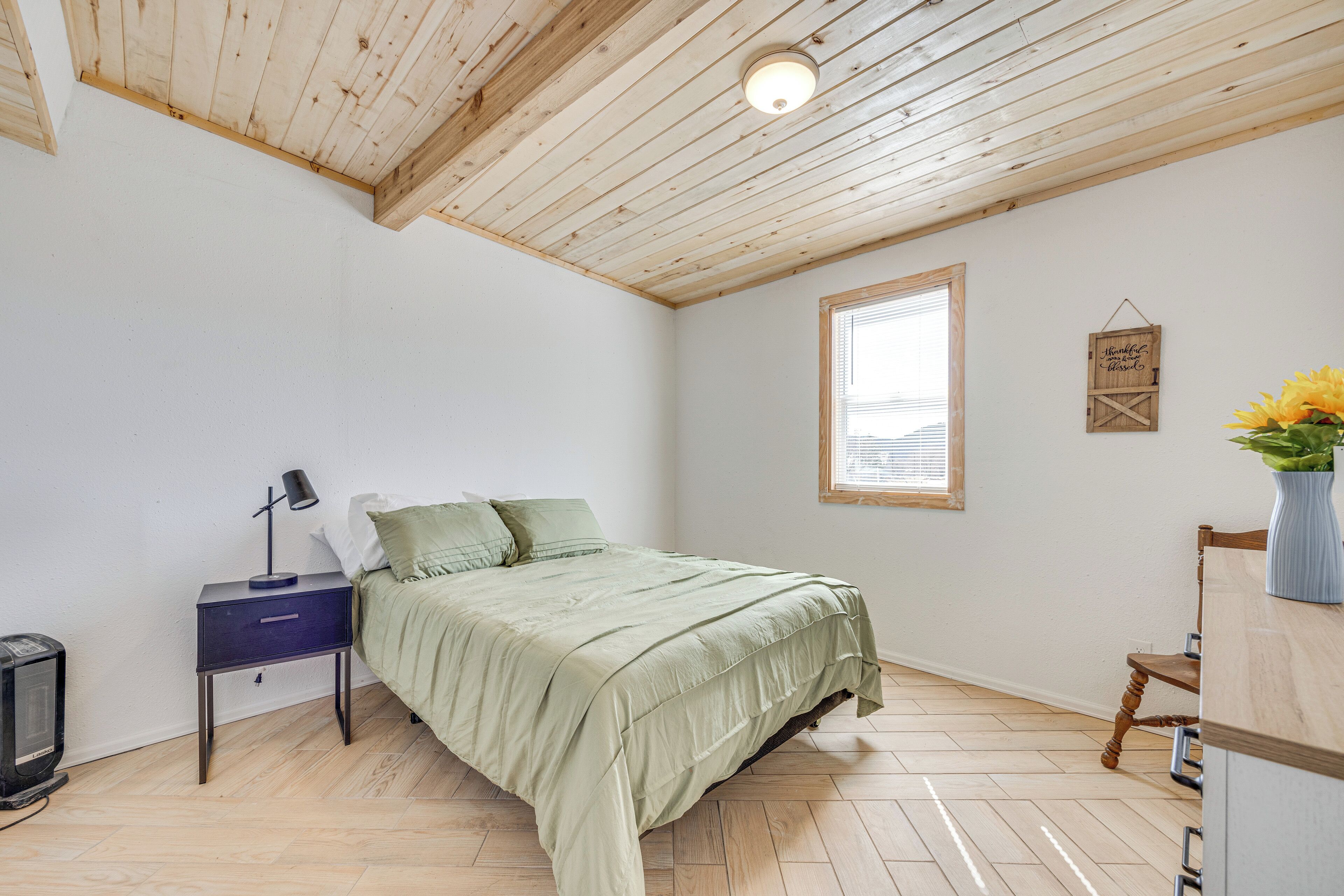 A bedroom with a bed, a nightstand, a lamp, a small table, and a window with blinds.