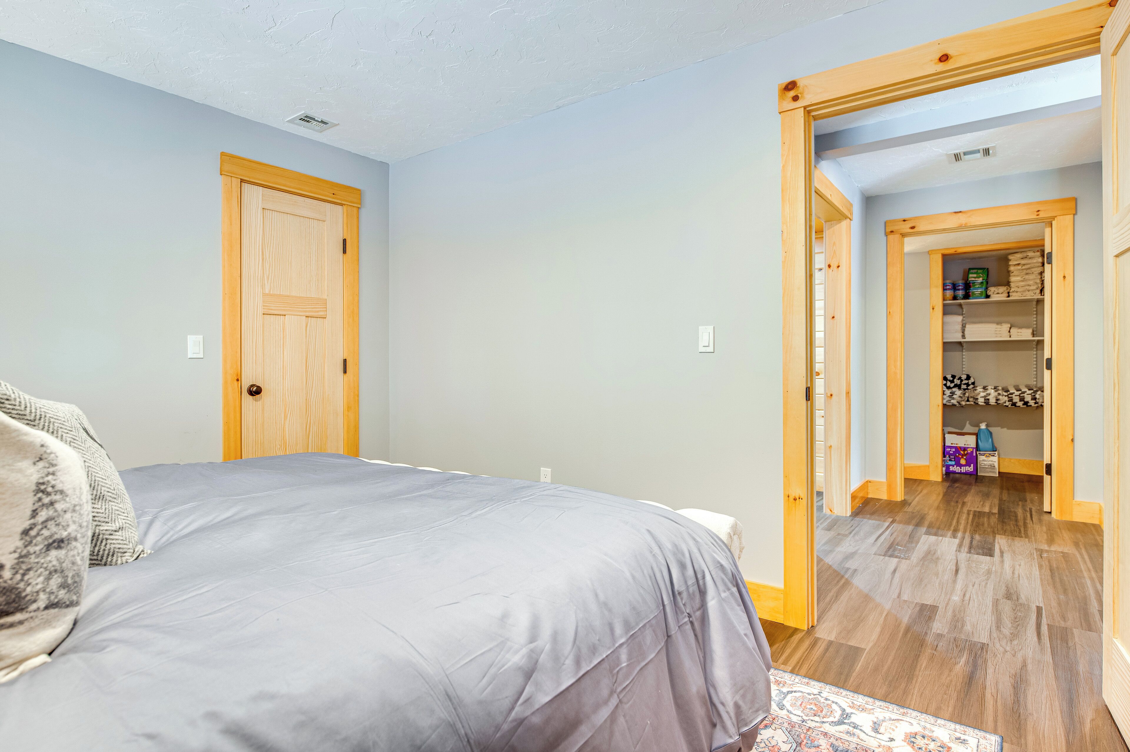 A bedroom with a bed, a wooden door, and a hallway leading to a storage area.