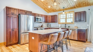A modern kitchen with wooden cabinets, stainless steel appliances, and a central island with bar stools. - 6 Mi to Lake Winnipesaukee: New Hampshire Home (Gilford)