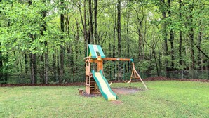 A playground with a slide and swing set in a grassy area surrounded by trees. - Ellijay Mtn Cabin w/ Hot Tub & Community Perks (Ellijay)