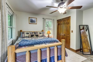A bedroom with a bed, a ceiling fan, a window with curtains, a wooden door, and a mirror.