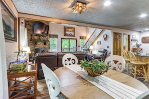 Un salon chaleureux avec une cheminée, un coin repas avec une table en bois et un escalier menant à un autre niveau.