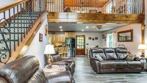 A spacious living area with leather sofas, a wooden staircase, and a kitchen in the background. - Ellijay Mtn Cabin w/ Hot Tub & Community Perks (Ellijay)