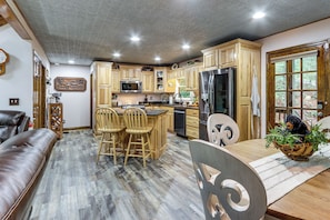 Une cuisine spacieuse dotée de meubles en bois, d’un îlot central avec des tabourets, d’un réfrigérateur et d’un coin repas comprenant une table et des chaises.