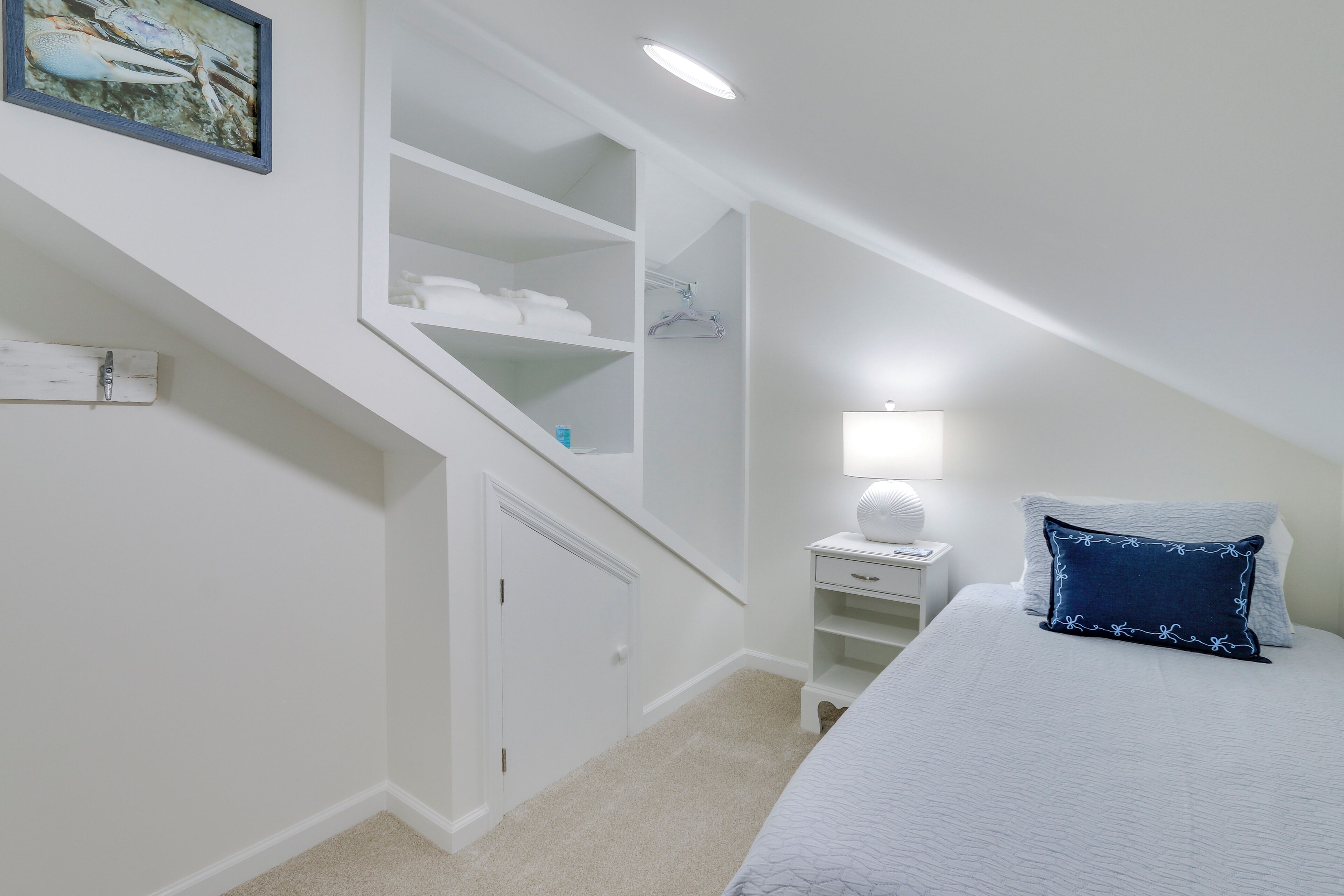 A bedroom with a bed, a nightstand, a lamp, a closet, and a staircase.