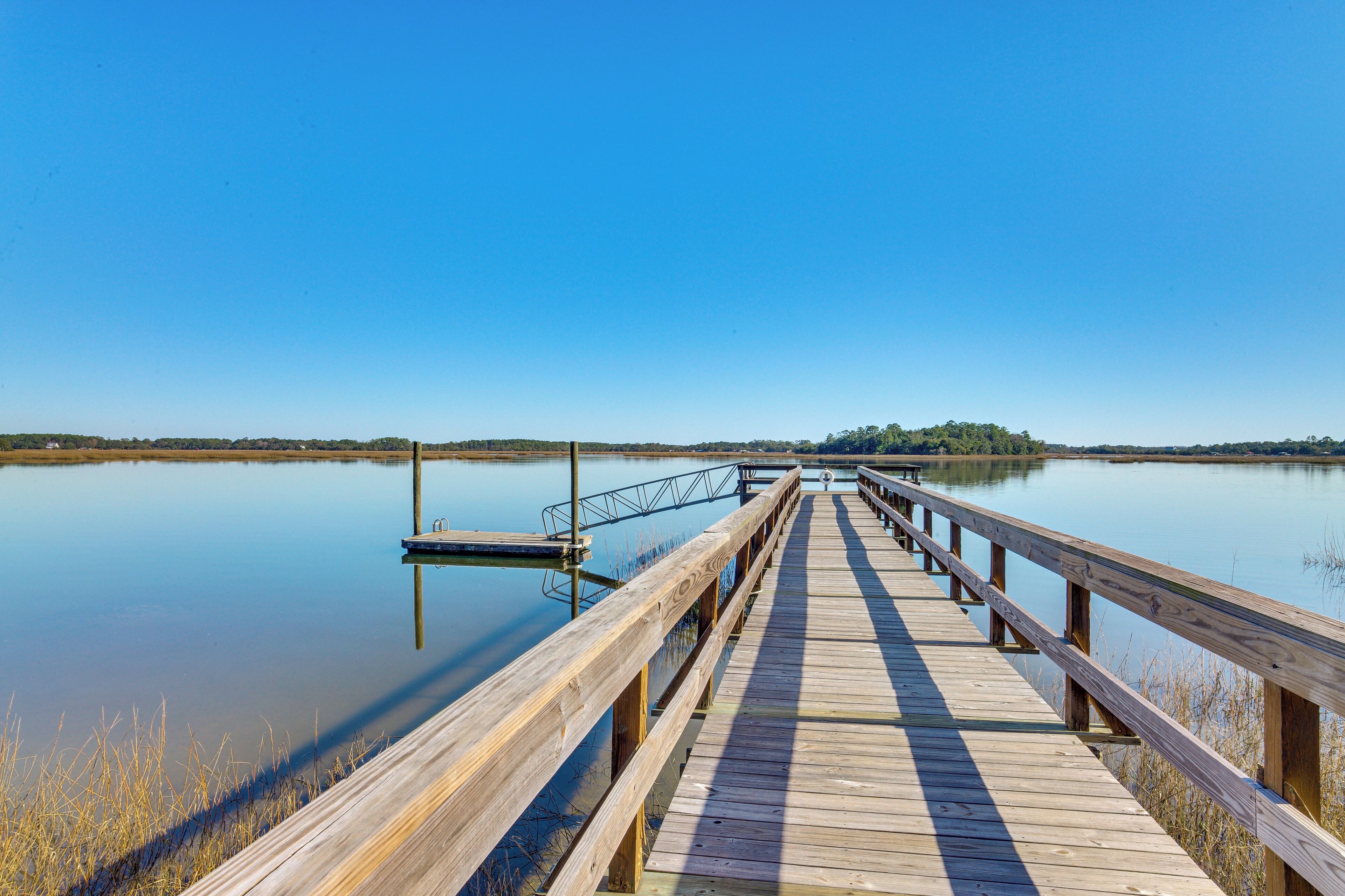 A wooden pier extending into calm water with a clear sky above.