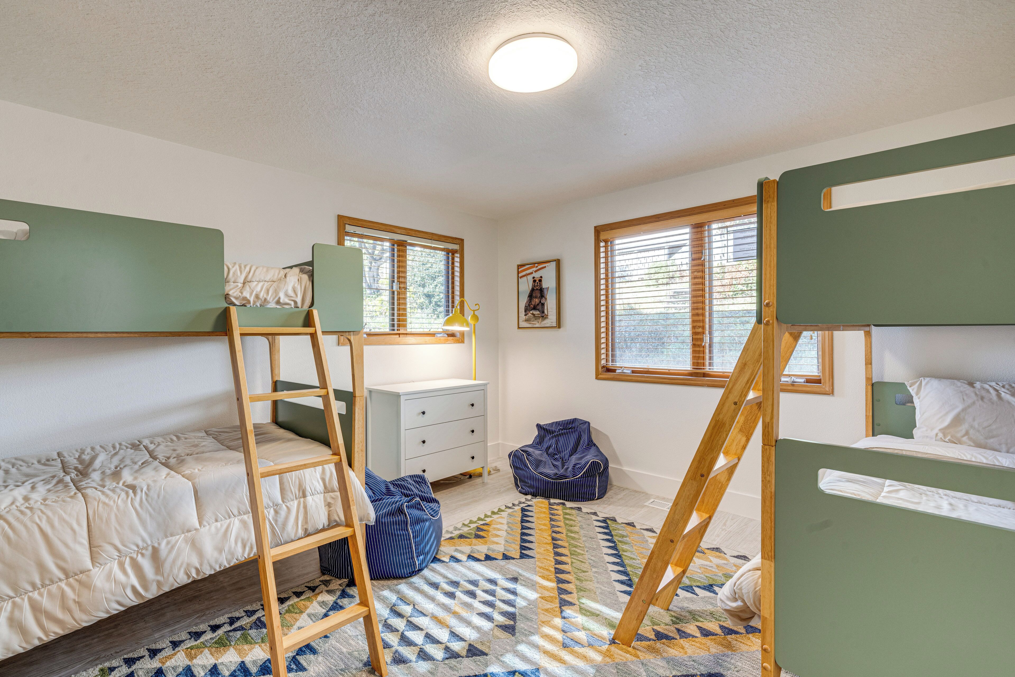 A room with bunk beds, a ladder, a desk, a chair, and a window with blinds.