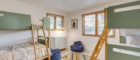 A room with bunk beds, a ladder, a desk, a chair, and a window with blinds.