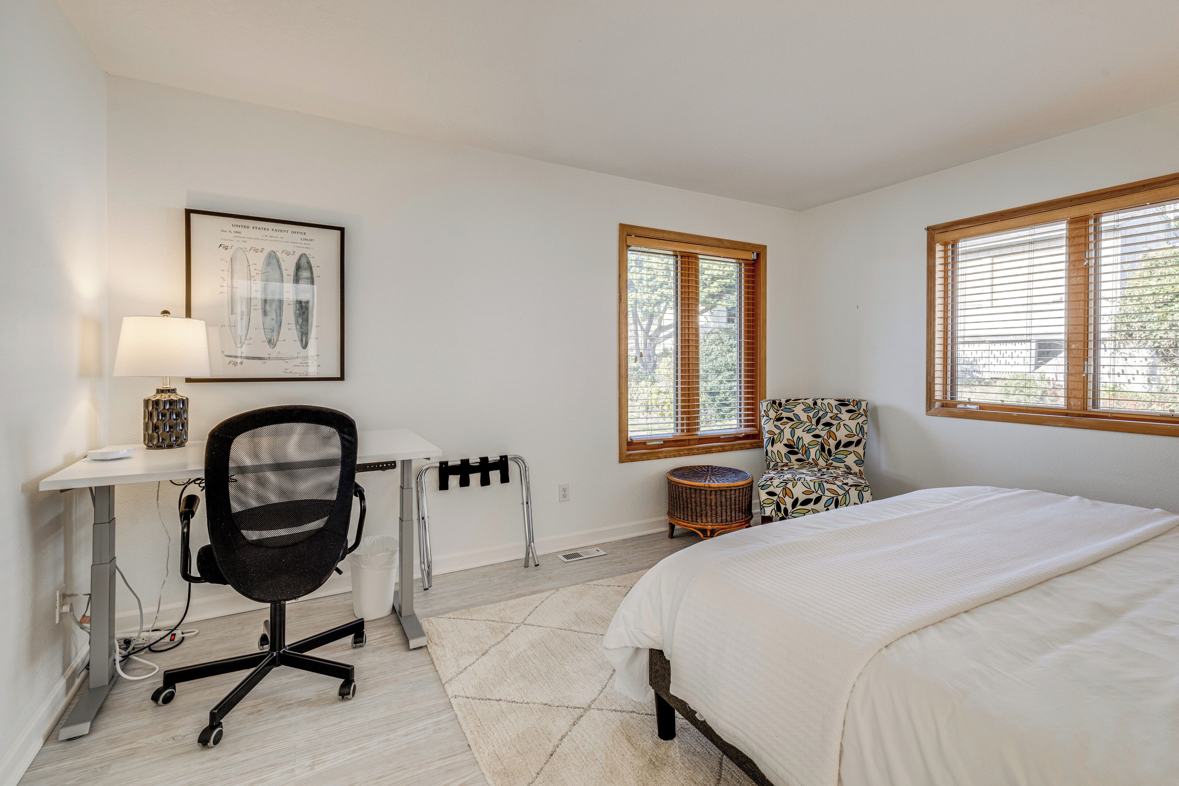 Une chambre à coucher avec un lit, un bureau et une chaise, une fenêtre avec des stores et un tableau encadré au mur.