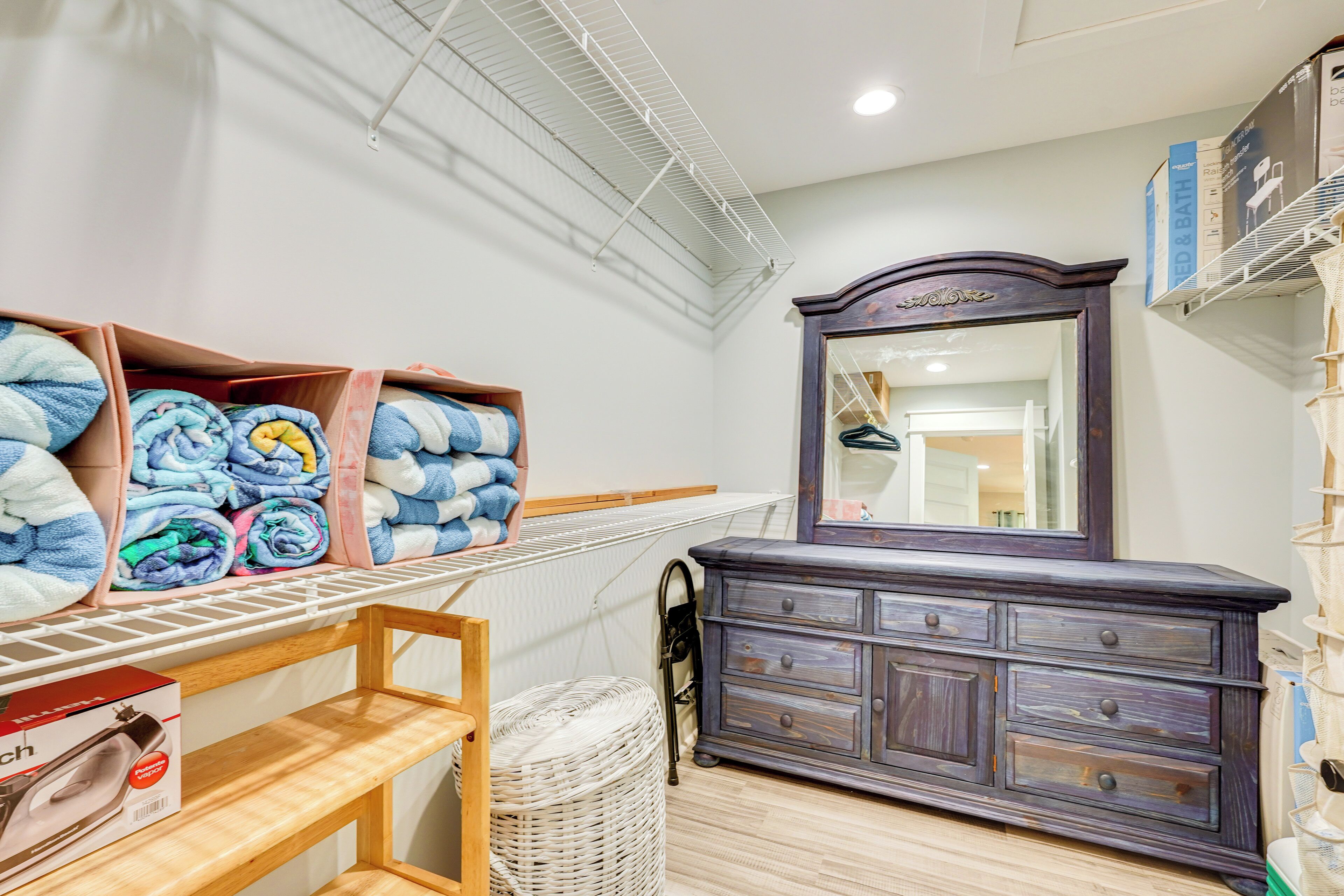 A laundry room with a drying rack, a wicker basket, a wooden shelf, and a dark wooden dresser with a mirror.