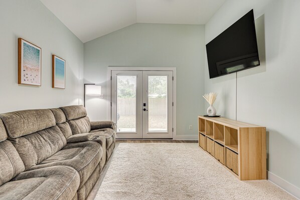 Una sala de estar con un sofá color beige, un televisor de pantalla plana montado en la pared y un mueble bajo de madera con cestas.
