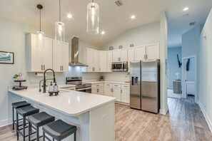 Une cuisine moderne avec des meubles blancs, des appareils en acier inoxydable et un îlot central doté de tabourets de bar.