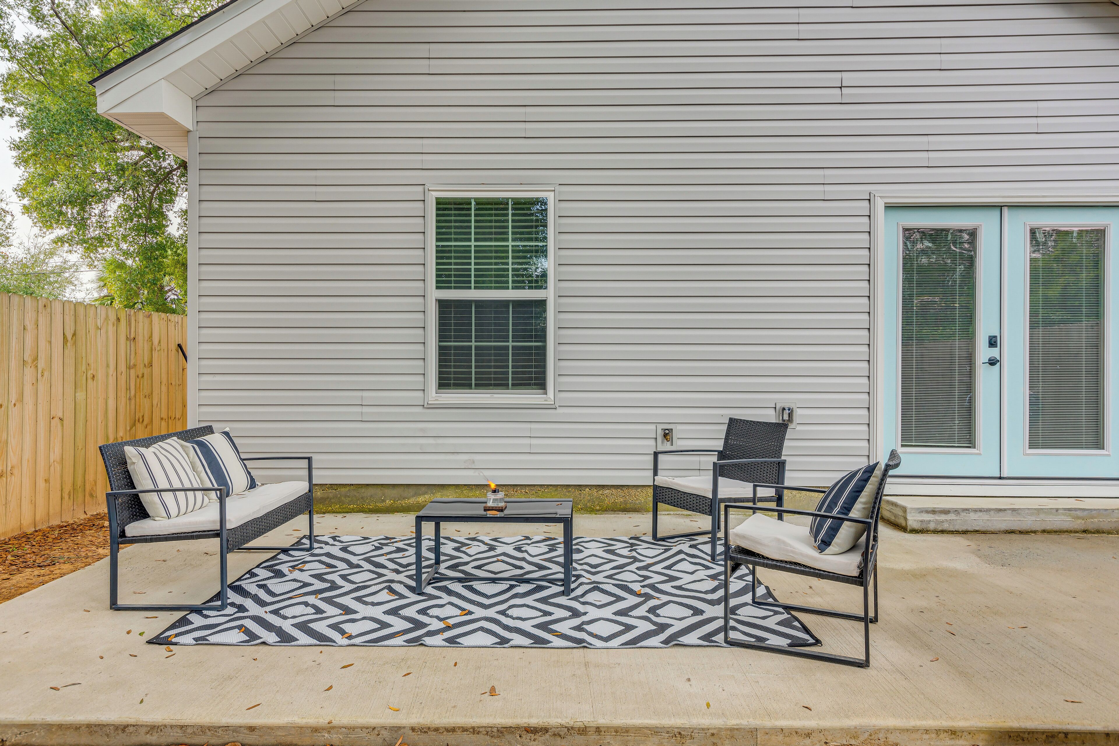 A patio with two chairs and a table, a wooden fence, and a house with a blue door and windows.