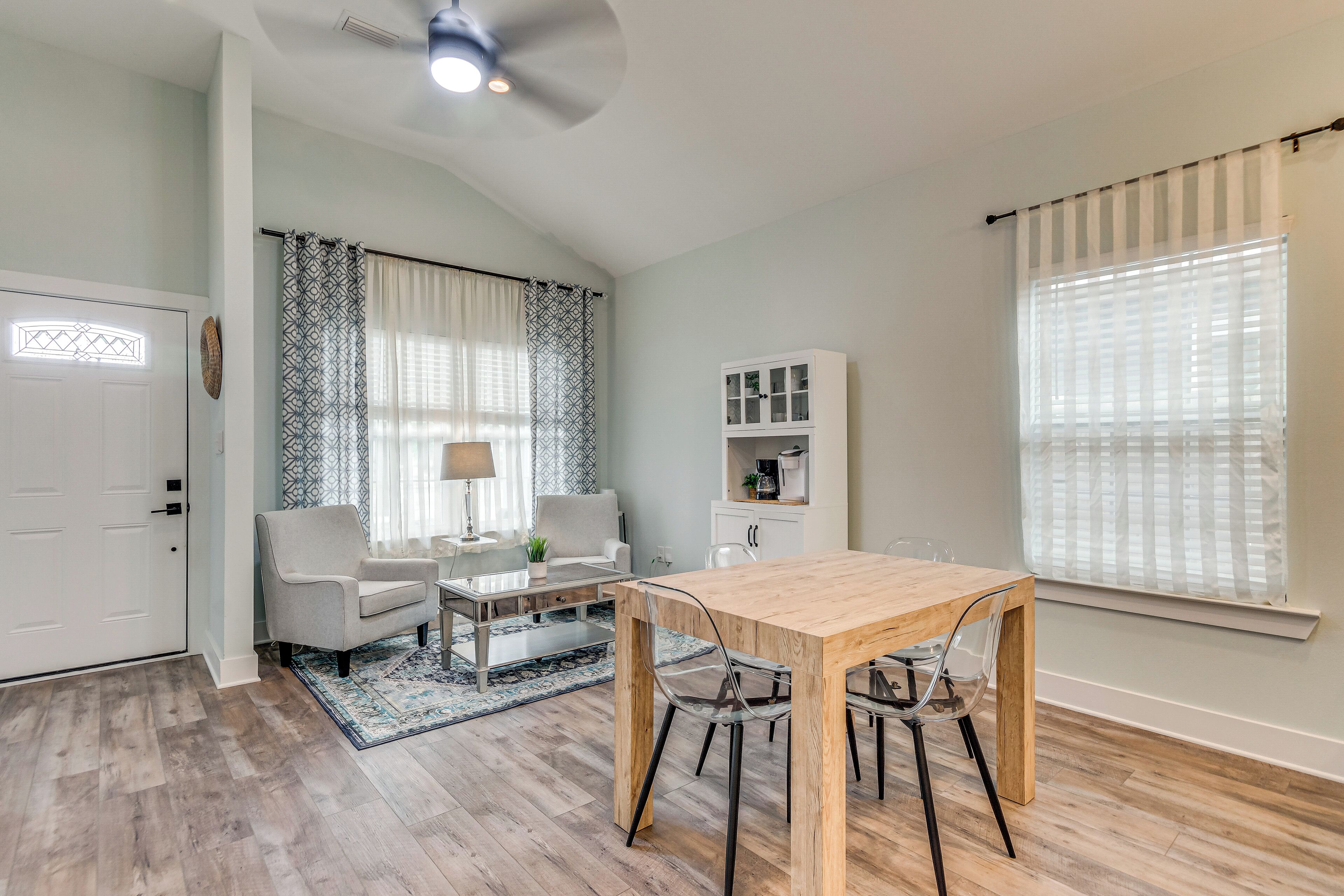 A modern living room with a wooden dining table, a sofa, a coffee table, and a patterned rug.