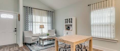 A modern living room with a wooden dining table, a sofa, a coffee table, and a patterned rug.