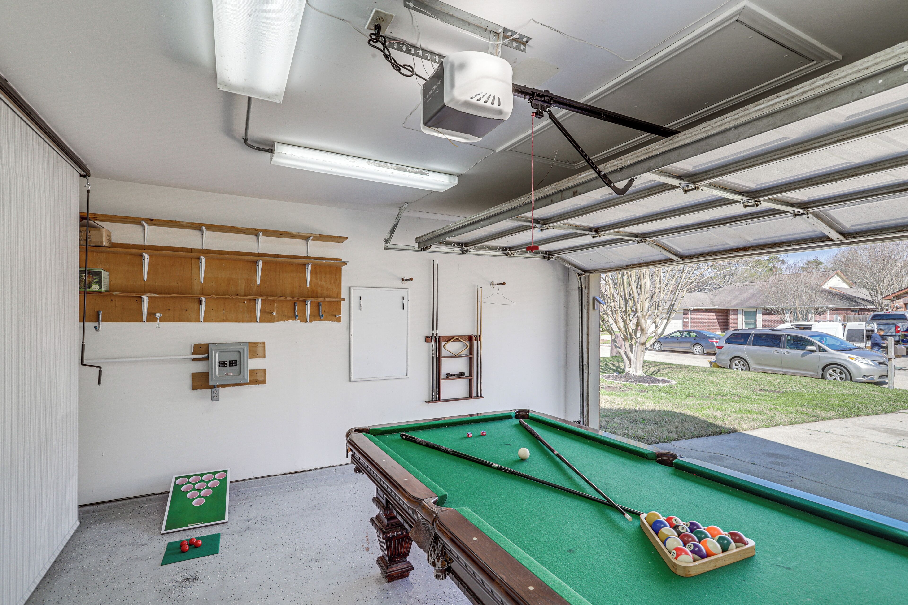 A pool table with balls, a green felt table, and a cue stick. There is a wooden shelf with hooks on the wall.