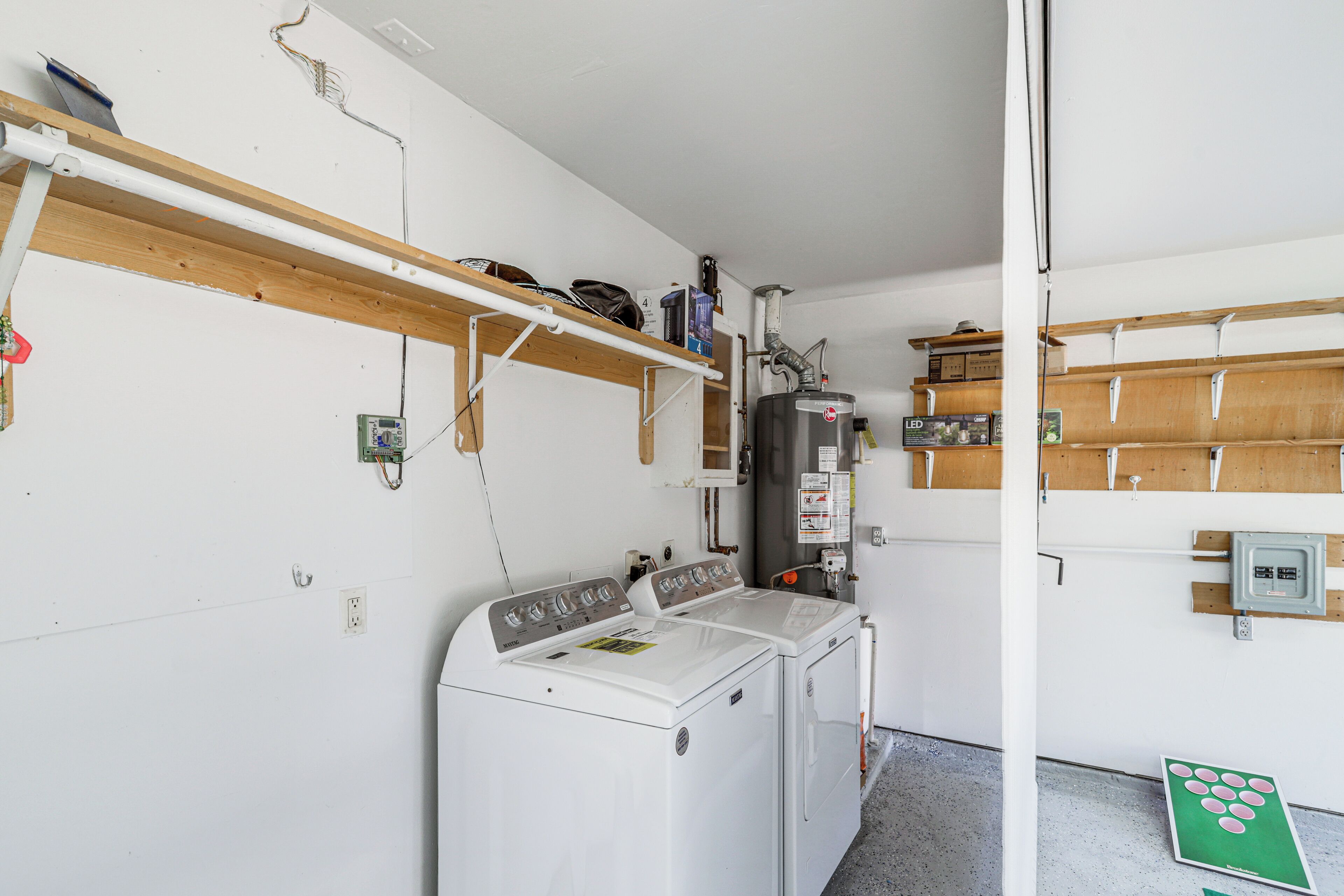 A laundry room with two washing machines, wooden shelves, and a utility room with a water heater.