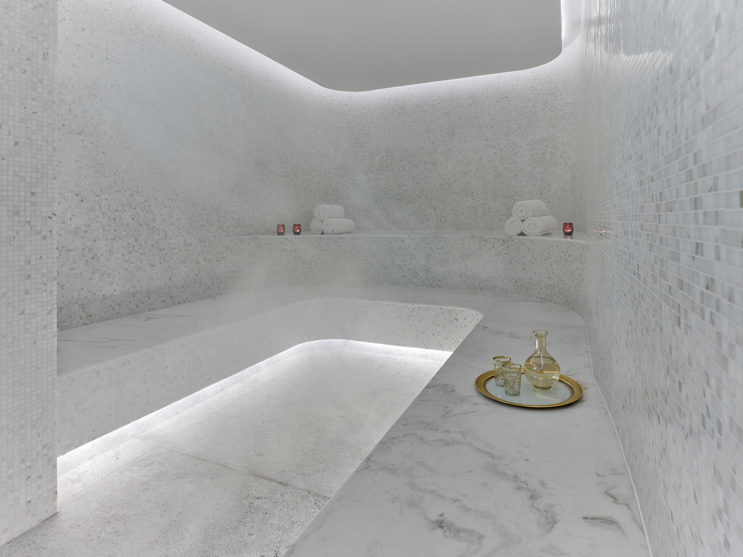 A modern bathroom with a large bathtub, a marble countertop, and a small shelf with decorative items.