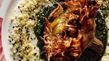 A plate of food with a roasted meat centerpiece, garnished with sesame seeds and herbs.