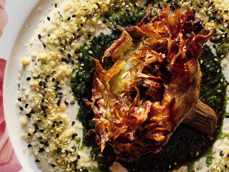 A plate of food with a roasted meat centerpiece, garnished with sesame seeds and herbs.