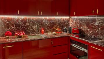 A modern kitchen with red cabinets, a marble backsplash, and stainless steel appliances.