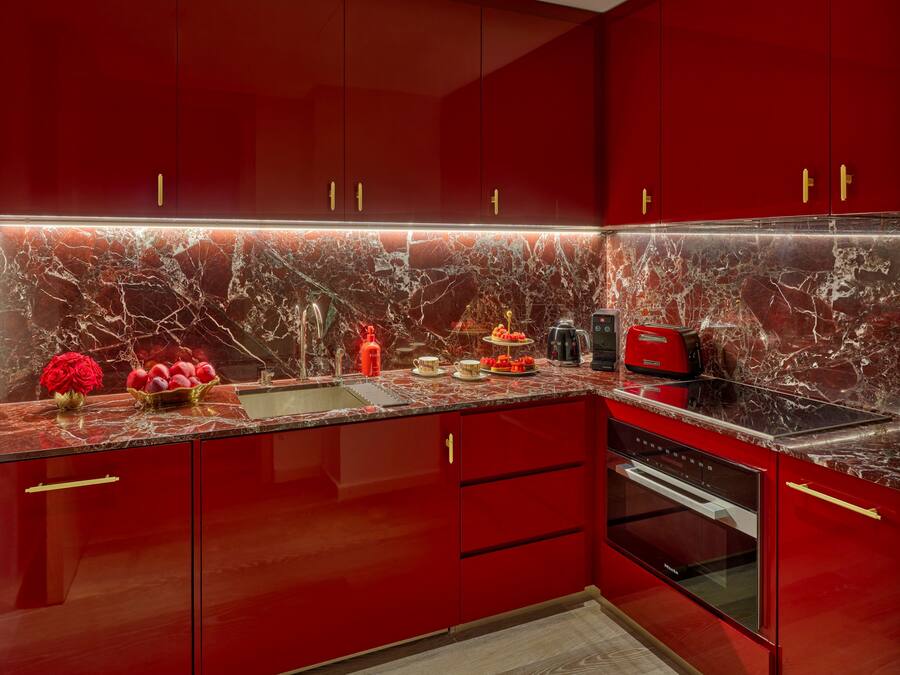 A modern kitchen with red cabinets, a marble backsplash, and stainless steel appliances.