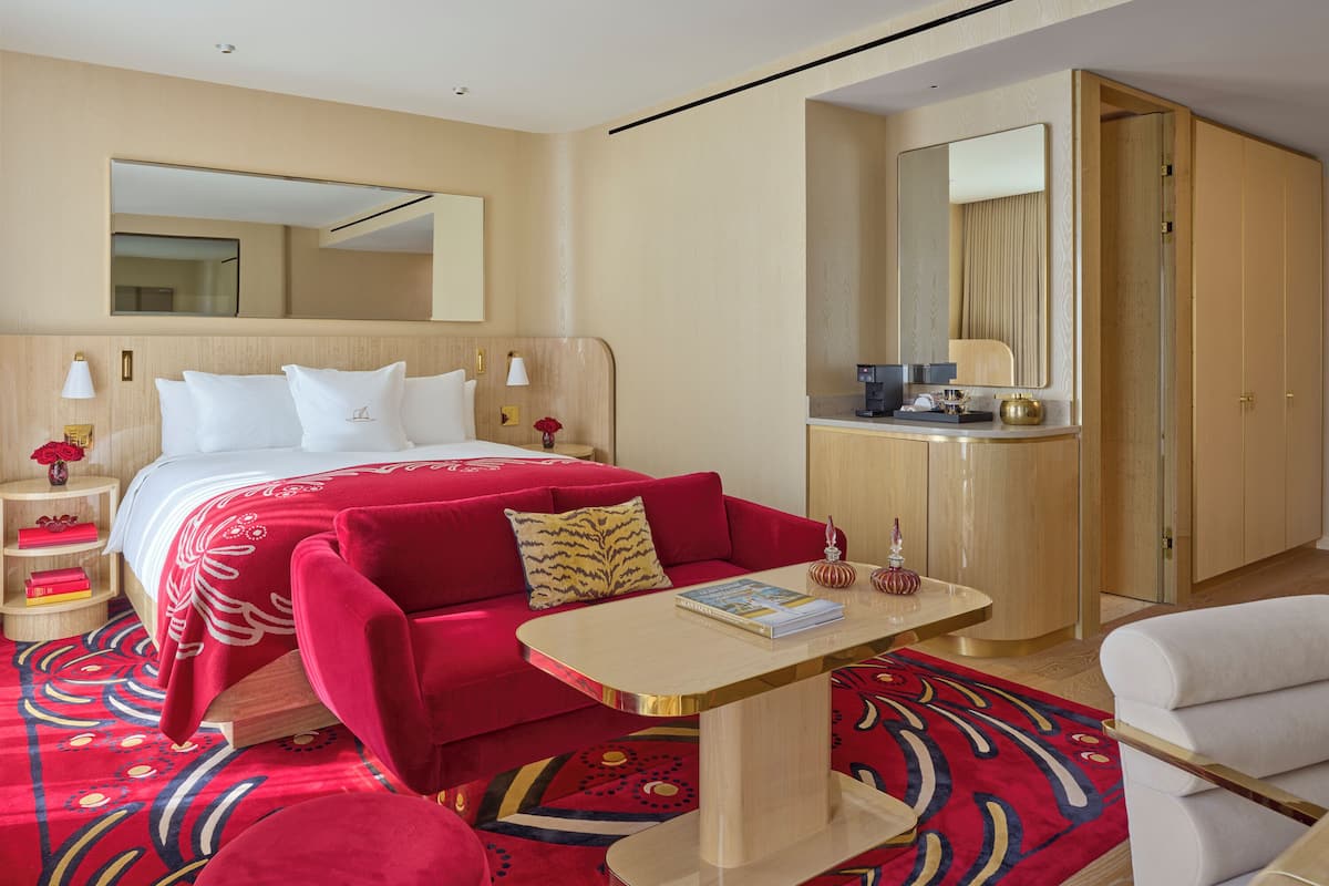 Habitación de hotel con cama, sofá rojo, una mesita, espejo, escritorio y armario.